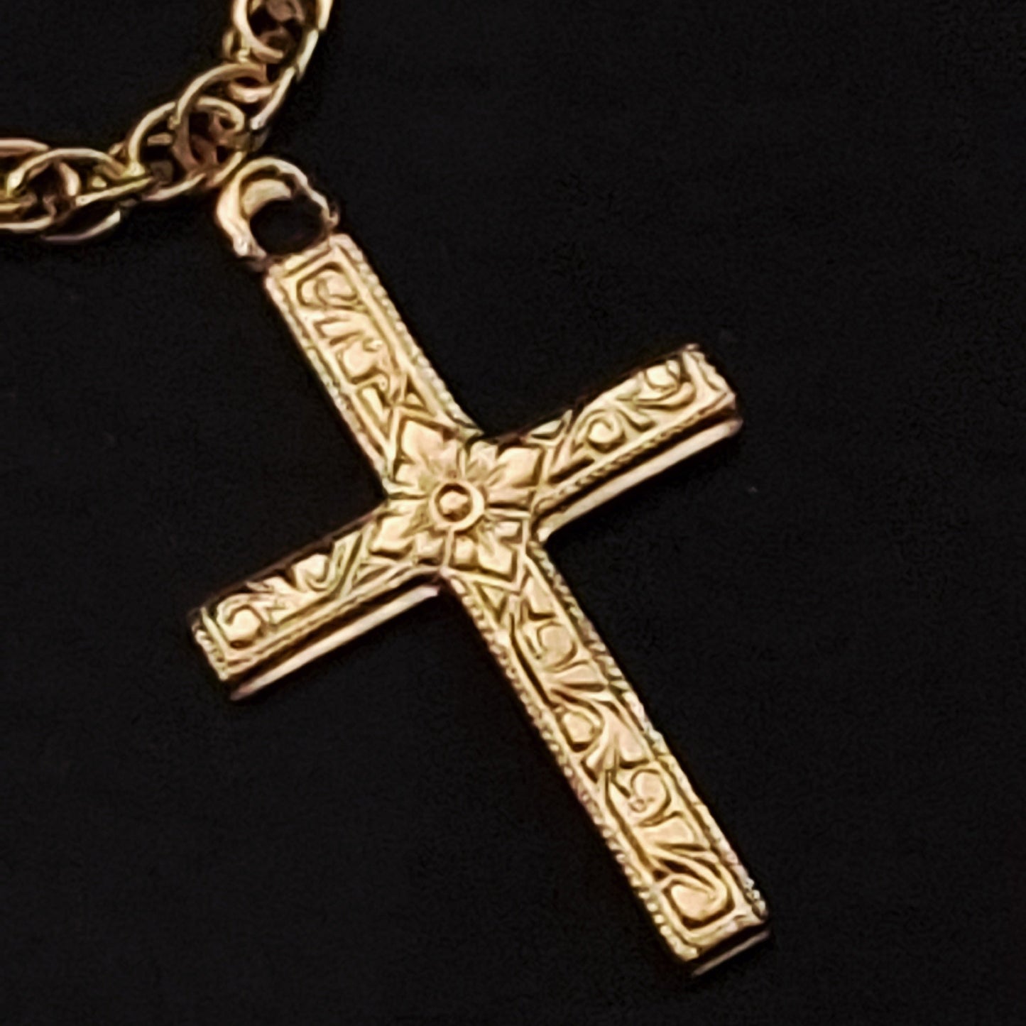 Gold cross pendant on a chain against a black background