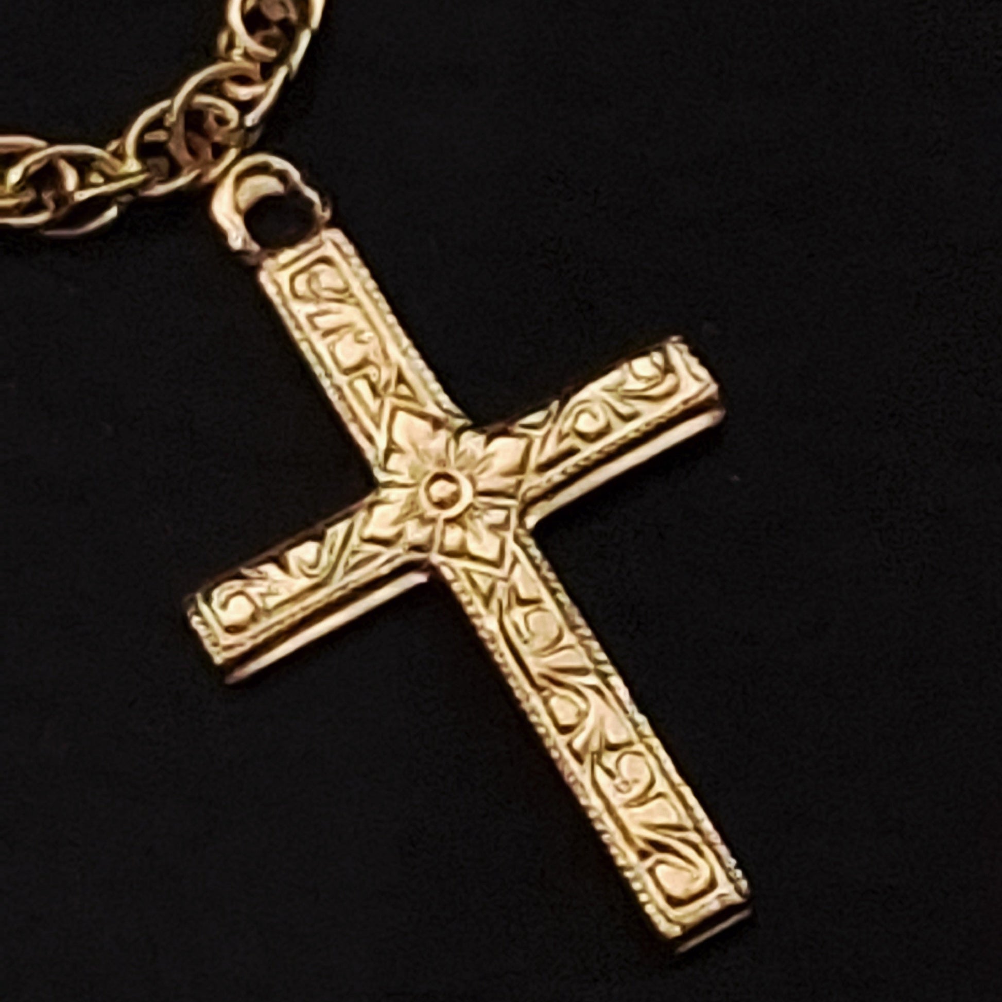 Gold cross pendant on a chain against a black background